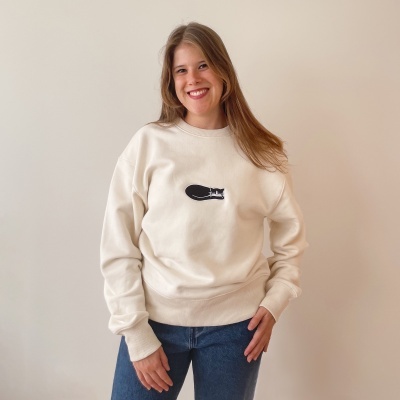 Mulher com sweatshirt creme com estampa de gato preto e calças de ganga azuis contra fundo branco