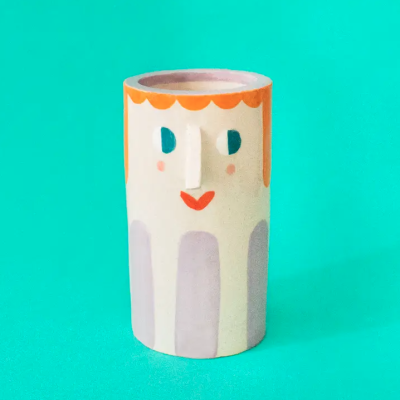 Vaso cilíndrico em cerâmica com rosto pintado em várias cores sobre fundo verde