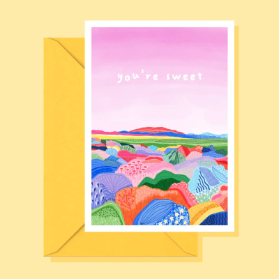 Cartão colorido com texto youre sweet e ilustração de colinas coloridas sobre fundo rosa, colocado em envelope amarelo