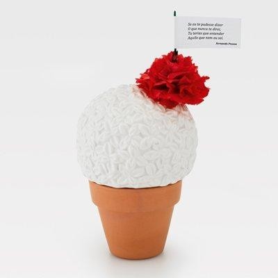 Planta decorativa artificial branca com flor vermelha em vaso de barro castanho e bandeira com texto em português