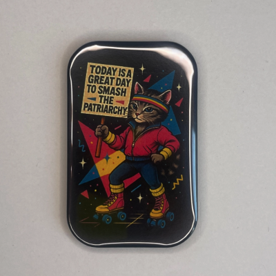 Pin metálico com imagem de gato em patins a segurar cartaz com texto motivacional.