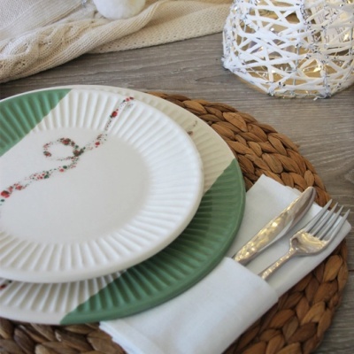 Conjunto de pratos cerâmicos decorados sobre sousplat de palha com talheres e guarda-napo branco
