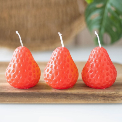 Três velas laranja em forma de morango sobre tábua de madeira