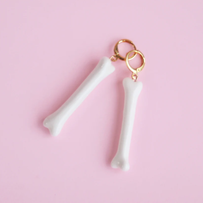 Brincos com pendentes em forma de ossos brancos brilhantes e argolas douradas sobre fundo rosa