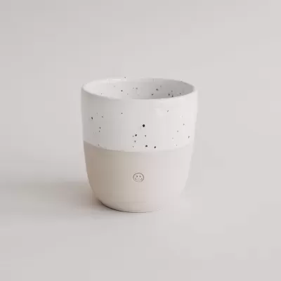 Caneca de cerâmica branca e bege com padrão manchado e símbolo de sorriso
