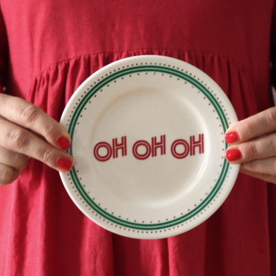 Prato branco com texto OH OH OH em vermelho segurado por mãos femininas com vestido vermelho