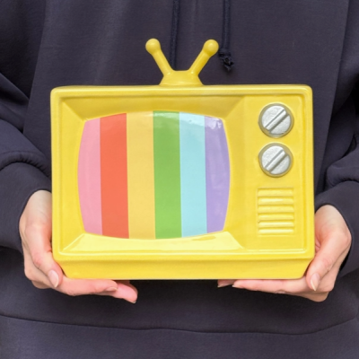 Placa decorativa amarela em forma de televisão vintage com ecrã colorido e botões prateados