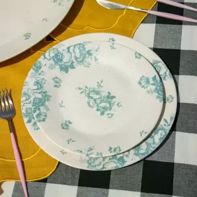 Pratos de cerâmica com padrão floral azul, talheres rosa e metal, guardanapo amarelo, toalha de mesa xadrez preta e branca