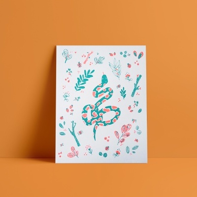 Cartaz com ilustração de uma serpente e motivos florais coloridos, apoiado numa superfície contra uma parede laranja
