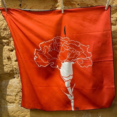 Lenço laranja com estampa branca e preta de flor grande e figura humana no topo.