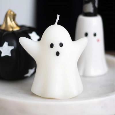 Vela branca fantasma com olhos e boca pretos numa superfície branca, abóbora preta decorada com estrelas ao fundo