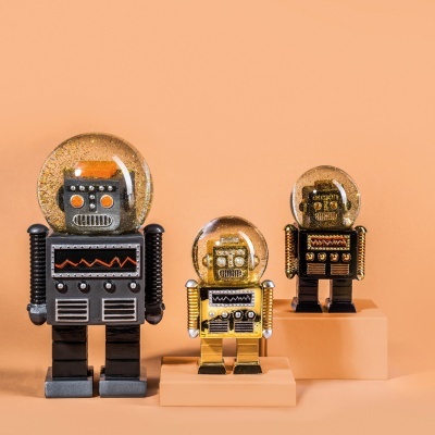 Três decorações de robôs vintage com cabeça transparente e glitter dourado em fundo cor de pêssego