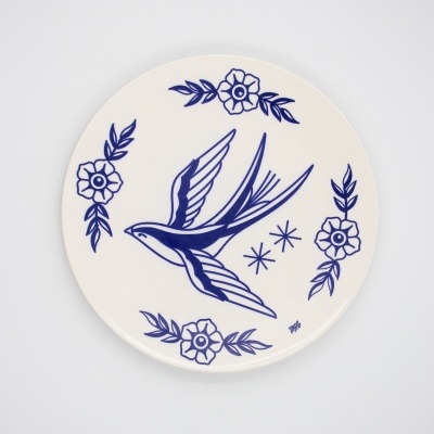 Prato cerâmico branco com desenho azul de andorinha e flores.