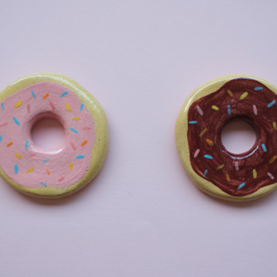 Dois donuts de cerâmica pintados com cobertura colorida sobre fundo rosa claro