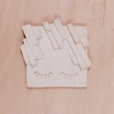 Objeto decorativo em cerâmica creme com olhos fechados sobre madeira clara