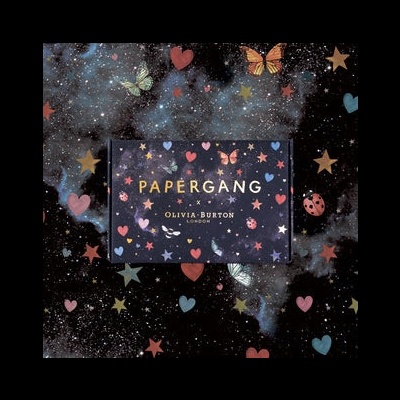Caixa azul escuro com texto PAPERGANG by OLIVIA BURTON LONDON e padrões de estrelas, corações e borboletas