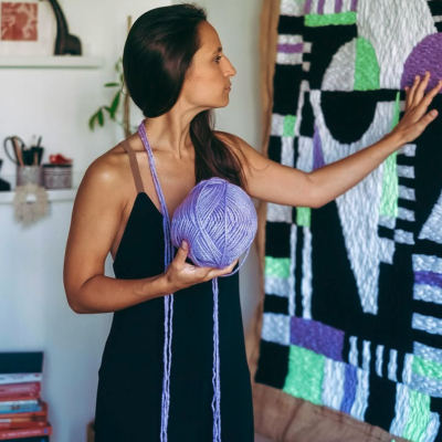 Mulher com novelo de lã lilás e tapeçaria geométrica colorida
