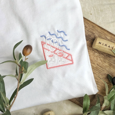 Tecido branco com bordado colorido e tábua de madeira com rolhas e ramos verdes