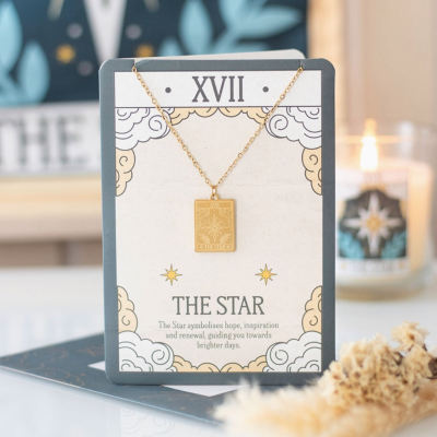 Colar dourado com pendente retangular gravado exposto em cartão decorativo com texto THE STAR