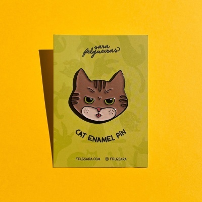 Pin esmaltado cabeça de gato numa cartolina verde sobre fundo amarelo