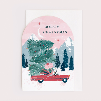 Cartão de Natal com ilustração de carro vermelho a transportar árvore de Natal e presentes, com montanhas e pinheiros ao fundo.