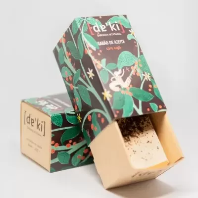 Sabonete artesanal embalagem ilustrada com texto 'de'ki SABÃO DE ACETE com café' e sabonete com grãos de café