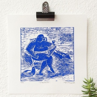 Gravura azul e branco de figura humana sentada numa cadeira com animal ao lado, pendurada numa parede branca.