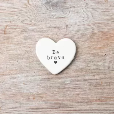Coração decorativo branco com texto 'Be brave' sobre madeira clara