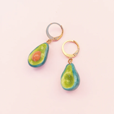 Brincos com pendentes em forma de abacate em fundo rosa
