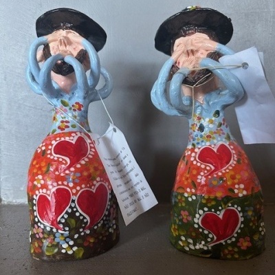 Duas figuras de cerâmica pintadas à mão com vestidos coloridos e corações vermelhos, tocando instrumentos azuis e usando chapéus pretos.