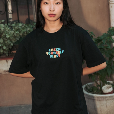 Mulher com t-shirt preta com texto colorido CHECK YOURSELF FIRST e calças azuis com padrão de corações