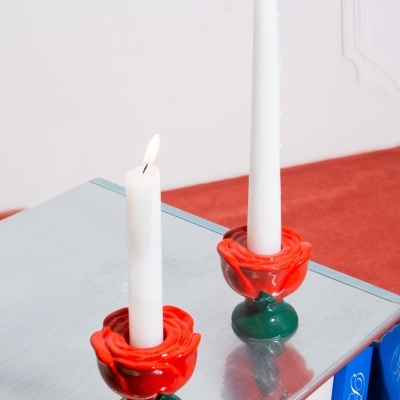 Dois castiçais em cerâmica em forma de rosa vermelha segurando velas brancas acesas numa superfície espelhada
