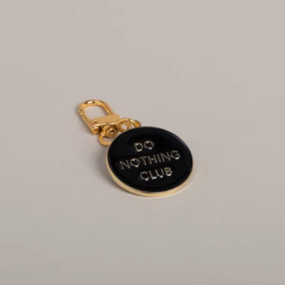 Chaveiro redondo em metal dourado com fundo preto e texto DO NOTHING CLUB