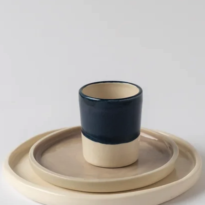 Conjunto de copo azul escuro e bege em pratos cerâmicos bege sobre fundo branco