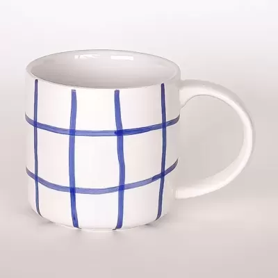 Caneca branca com padrão de riscas azuis formando uma grelha