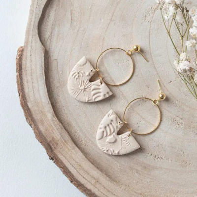 Brincos com pendentes de argila branca texturizada em prato de madeira e flores pequenas