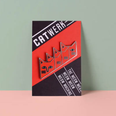 Pin de metal com design de quatro gatos em cartolina vermelha e preta com texto CATWERK