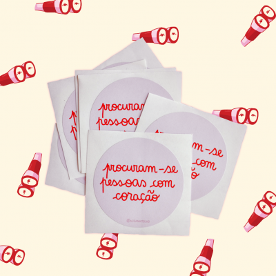 Autocolantes redondos com texto vermelho 'procuram-se pessoas com coração' em fundo branco, sobre um fundo bege com lanternas vermelhas desenhadas.