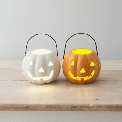 Duas abóboras decorativas de Halloween iluminadas, branca e laranja, em cerâmica com alça de metal sobre mesa de madeira