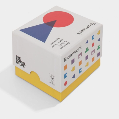 Embalagem cúbica branca e amarela com padrões geométricos coloridos e textos em português e inglês