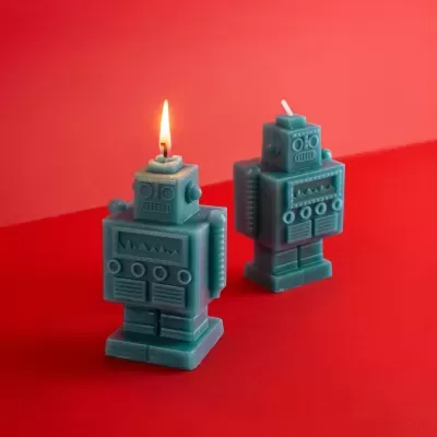 Duas velas em forma de robô azuis em superfície vermelha, uma acesa.