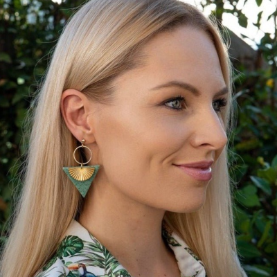 Brincos pendentes dourados e verdes em mulher com camisa estampada em fundo de plantas