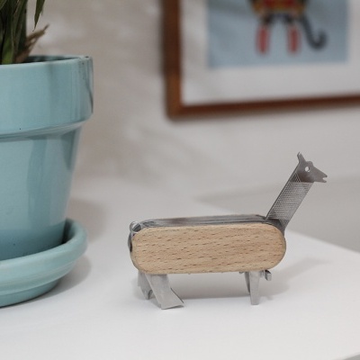 Figura decorativa de girafa em madeira e metal ao lado de vaso azul claro sobre mesa branca