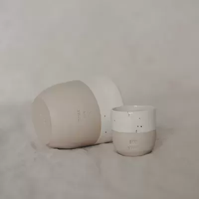 Três vasos de cerâmica bege e branco empilhados sobre tecido cinzento