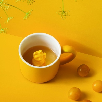 Caneca amarela com figura de gato no interior sobre fundo amarelo com bolas e flores