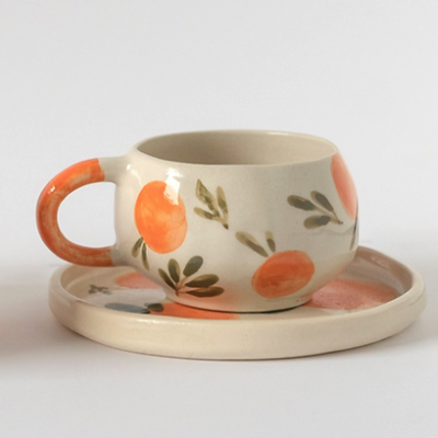 chávena de cerâmica com padrão de laranjas e folhas verdes sobre prato