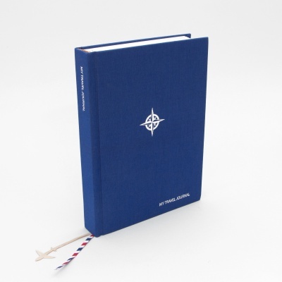 Caderno azul com bússola branca e texto 'MY TRAVEL JOURNAL' em fundo branco
