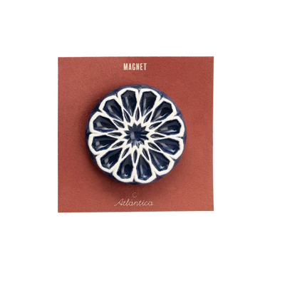 Íman redondo azul e branco com padrão geométrico num cartão castanho