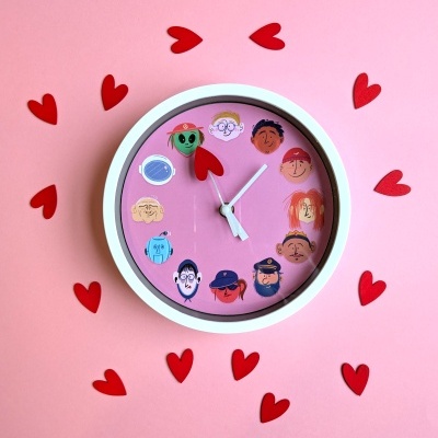 Relógio de parede cor-de-rosa com caricaturas e ponteiro de coração rodeado por corações vermelhos