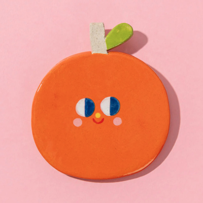 Objeto decorativo em forma de tangerina com rosto, fundo rosa